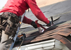 A Hartford roofing expert nailing new roof shingles down on a home. 